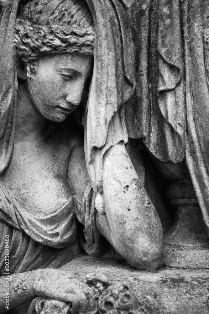 Fototapeta premium Ancient cemetery sculpture with bowed head in monochrome composition