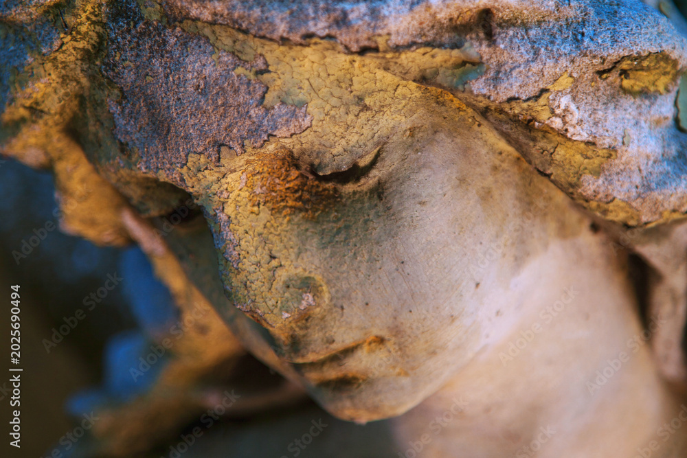 Fototapeta premium Weathered angel statue with bowed head and warm dramatic lighting