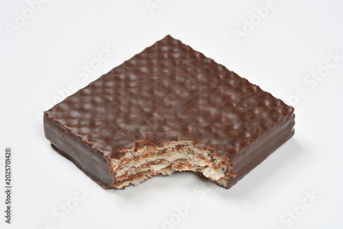 An angled view of a square chocolate coated wafer with a bite taken out showing internal layers and cream filling on a white background