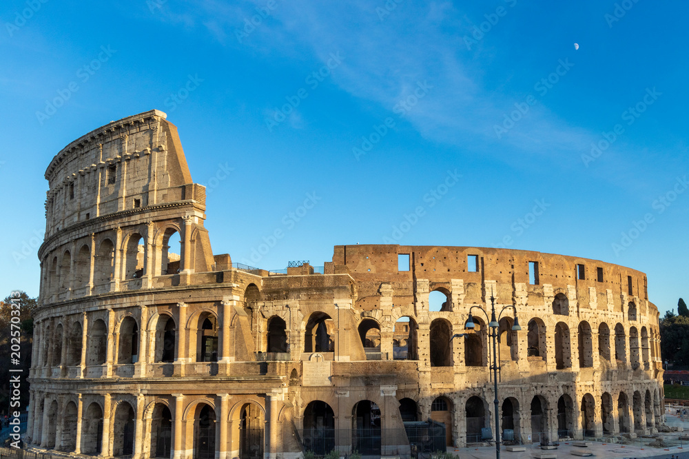 Obraz premium Famous Coliseum in Rome. Colosseum, or Coliseum. Sunset at huge Roman amphitheatre, Rome, Italy, Europe. Famous touristic place in the world and Europe. Beautiful blue sky background.