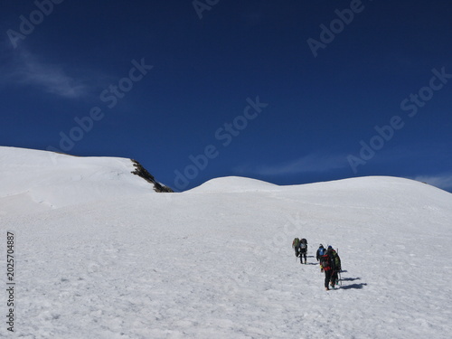 A group of mountaineers rope team climbing a snowy slope towards the summit under a deep blue sky, concept of teamwork, leadership, and joint achievement in Himalayas.