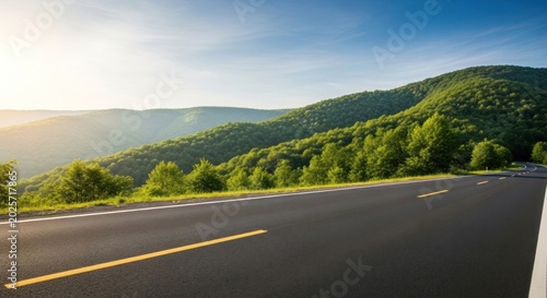 Empty asphalt highway road stretching through a lush green mountain forest landscape under a bright blue sky on a sunny summer day