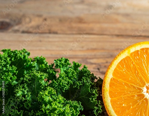 Kale foliage and orange slice placed on wooden table surface