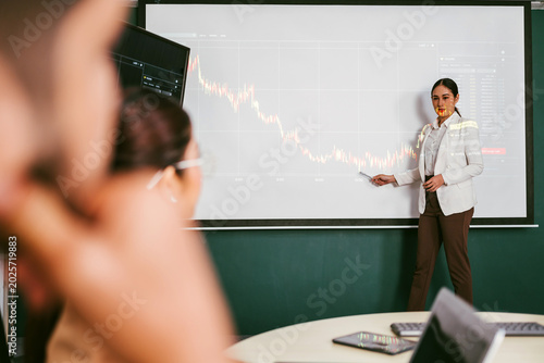 Professional presents a financial chart to colleagues in a meeting room, pointing at a declining line on a large screen during a business analytics presentation