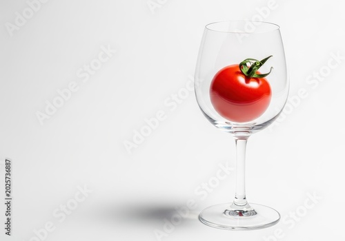 Vibrant red cherry tomato artfully displayed inside a crystal clear stemmed wine glass on a white background, highlighting freshness, cherry tomato, whole, fruit