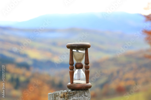 Vintage hourglass on weathered post with autumn landscape background