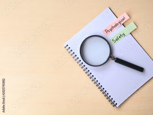 Psychological safety concept on a adhesive note with book and magnifying glass on wooden desk. Representing workplace culture, mental health, and teamwork 