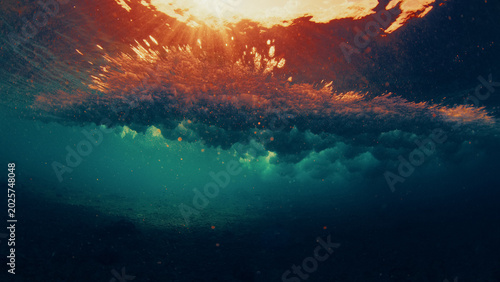 Underwater view of a breaking ocean wave with golden sunset light reflecting through the water surface and dynamic textures.