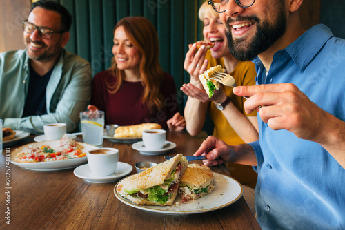 Friends eating sandwiches and drinking coffee at restaurant table