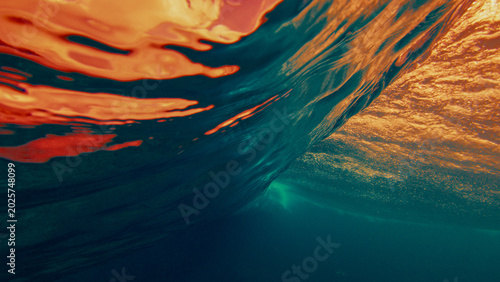 Underwater view of a breaking ocean wave with golden sunset light reflecting through the water surface and dynamic textures.