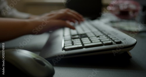 Close up view of hands typing on a black computer keyboard and operating a mouse on a dark desk surface