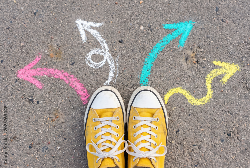 Fototapeta premium Person standing on asphalt with colorful chalk arrows showing multiple paths