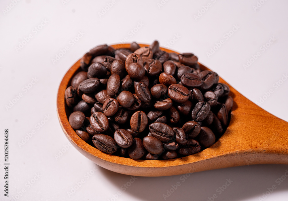 Fototapeta premium Close-up of roasted coffee beans in a wooden spoon on a wooden table with dark background, showcasing rich aroma and premium coffee concept.