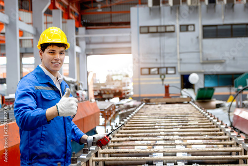 Tableau sur toile Male worker wearing safety clothing and helmet giving thump up during operating machinery at manufacturing factory