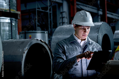 Fotografía Young worker with tablet inspecting large metal tubes at factory during night shift