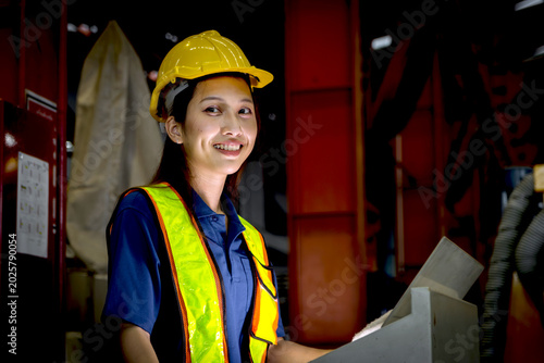Fotografía Happy Asian female worker using computer to operate machinery at manufacturing factory during night shift