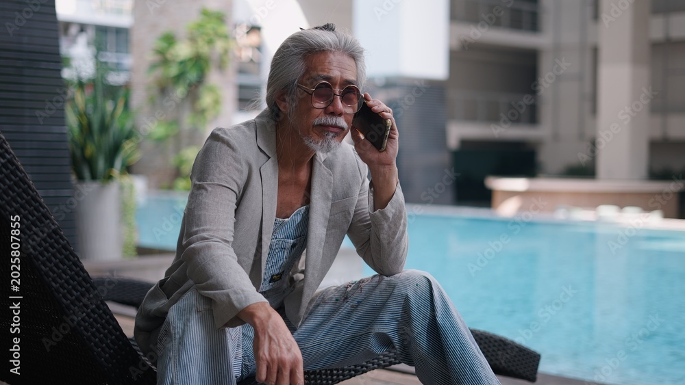Fototapeta premium Senior asian man making phone call by pool embodying modern lifestyle