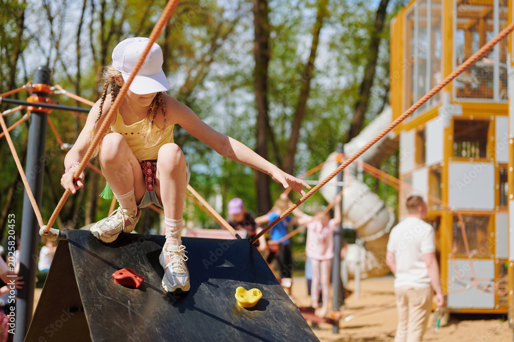 Obraz premium Young girl climbing on outdoor playground structure in park.