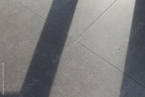 Geometric shadows cast across textured gray concrete tiles on a sunny day