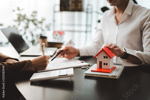 Real estate agent assisting client signing purchase contract for new home, discussing property ownership and investment, securing mortgage loan and insurance policy