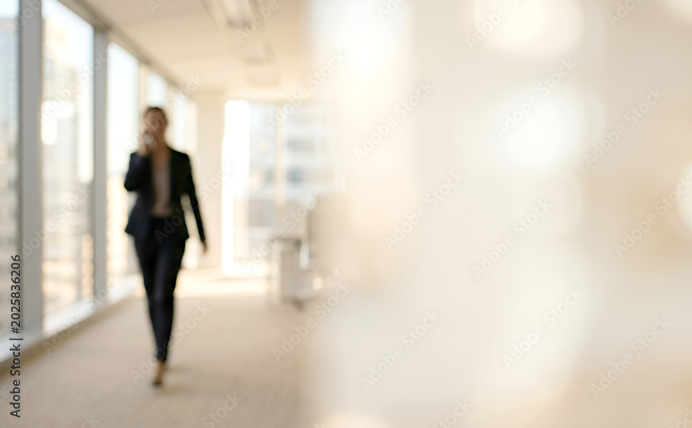 Fototapeta premium A blurred image of a businesswoman walking in a modern office corridor while speaking on her phone, emphasizing a professional work environment.