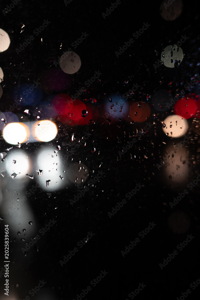 Fototapeta premium Rain on Window at Night with Blurred City Lights. Moody Urban Background. Raindrops
