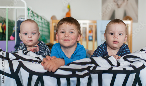 Canvastavla Three innocent gazes emerge from soft covers a smiling big brother watches over