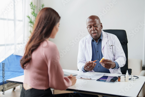 African American doctor discussing medication and treatment options with an Asian female patient, providing guidance during a medical consultation in a clinic office