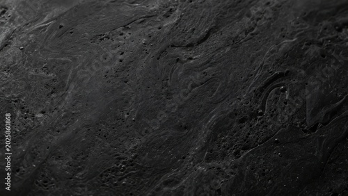 Dark black liquid paint surface with swirling patterns and glossy wet texture for abstract background