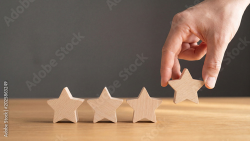 A hand places a wooden star, completing a four-star rating. Represents positive customer reviews, feedback, and excellent service