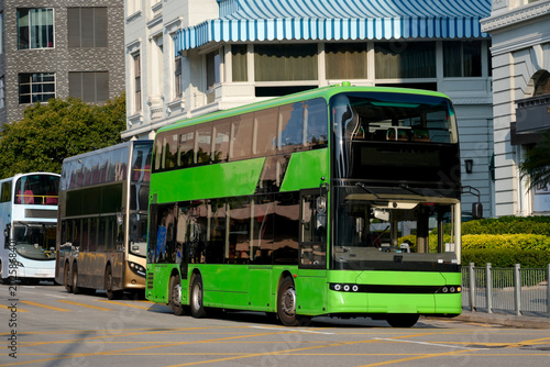 A row of double-decker buses of different colors on the side of a city street. The first one is green.