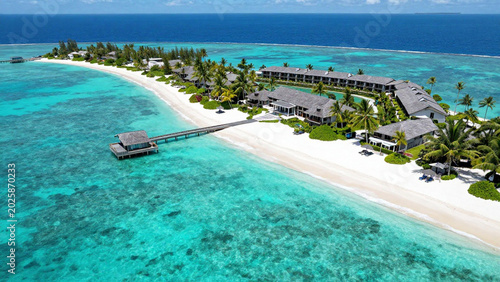 Aerial View of Luxury Tropical Island Resort with Overwater Villas. Beautiful aerial drone view of tropical island resort with overwater villas surrounded by turquoise lagoon and crystal clear ocean.