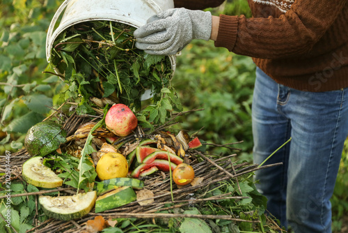 Food waste, scrap of vegetables and fruits in bucket with grass for compost close up. Farmer composting in compost heap pile, zero waste concept