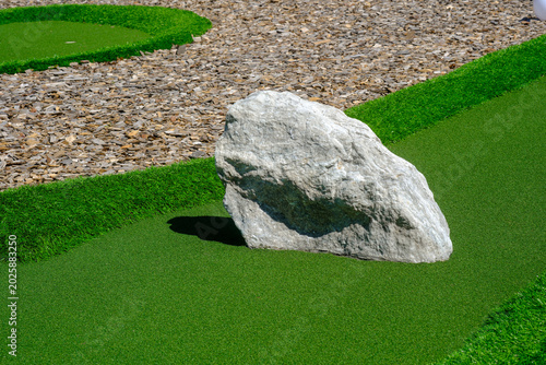 Large rock on a green golf field next to gravel