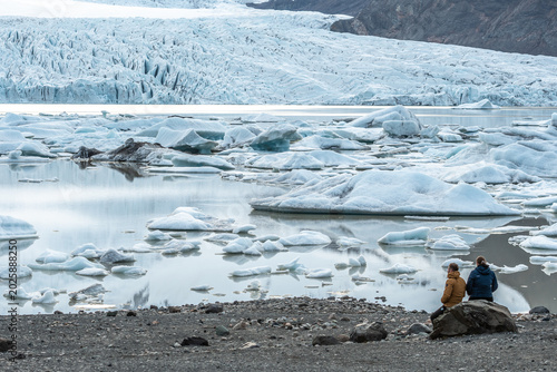 A couple of tourists admiring the glacier lagoon with icebergs at the foot of the Vatnajokull Glacier or Vatna Glacier, the largest and most voluminous ice cap in Iceland