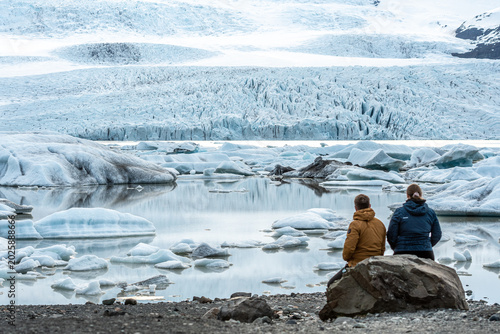 A couple of tourists admiring the glacier lagoon with icebergs at the foot of the Vatnajokull Glacier or Vatna Glacier, the largest and most voluminous ice cap in Iceland