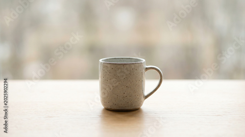 Speckled ceramic mug resting on a light wooden table with blurred view