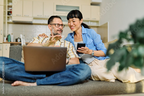 Portrait of a lovely young couple using a laptop and a mobile phone  together and having fun sitting on sofa at home