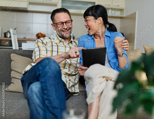Portrait of a lovely young couple using a tablet computer together and having fun sitting on sofa at home