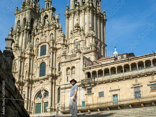 Happy man in a fedora hat and sunglasses smiling in front of Santiago de Compostela Cathedral.