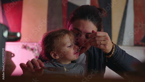 Slika na platnu Mother pretending to eat spoonful before toddler grabs bite, playful mealtime in