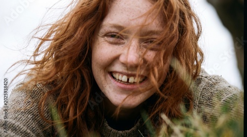 Close up low angle smiling redhead woman with freckles and wind blown hair for candid portrait lifestyle background and warm expressive banner design