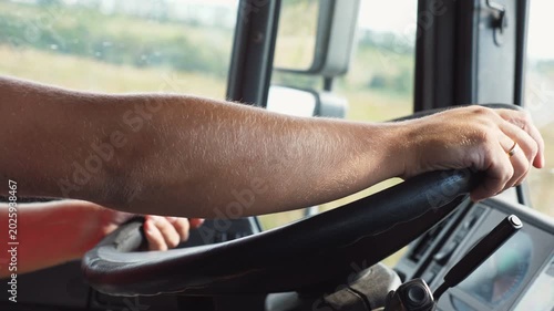 Male hands of trucker holds a big steering wheel while operating a truck through countryside. Lorry driver riding to destination at country road. Concept of logistics and transportation. Close up