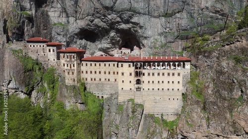 Aerial establishing shot of Sumela Monastery facade, Trabzon. Front drone view highlighting the iconic architecture of the ancient rock-hewn sanctuary built on a mountain precipice