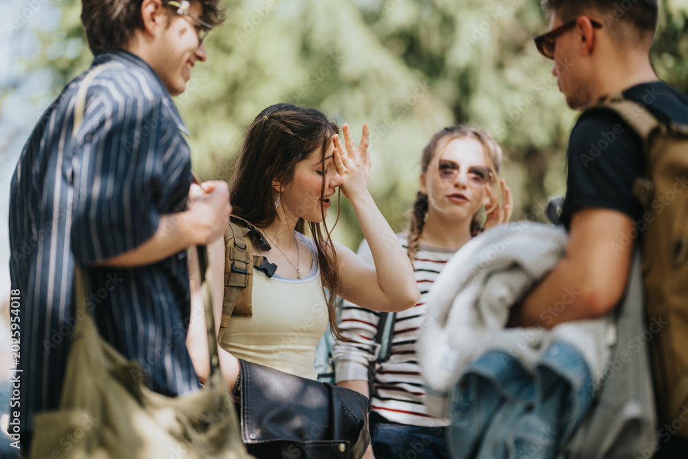 Fototapeta premium A group of teenage friends talk and laugh together in an outdoor setting. The young people socialize casually while carrying backpacks and jackets.