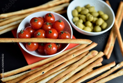 Bild auf Leinwand Bowl of cherry tomatoes, green olives, and grissinis breadsticks