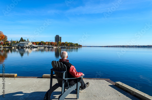 Senior male adult sitting on an Adirondack chair facing a marina on the opposite shore
