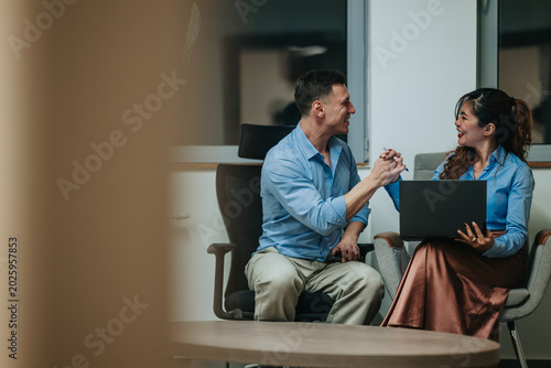 Fotografía Two business teammates celebrate a small success while talking and shaking hands in an office