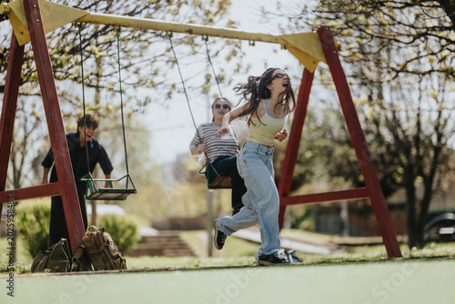 Cuadro en lienzo Three friends enjoy playful moments on swings at a sunny neighborhood playground