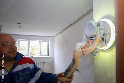 Tableau sur toile A professional worker wearing protective glasses uses a handheld drywall sander with built-in LED lighting to smooth a wall